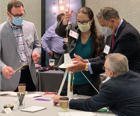Dr. Jacobs (right, standing) engages with METS participants and faculty in a tower-building ice breaker challenge