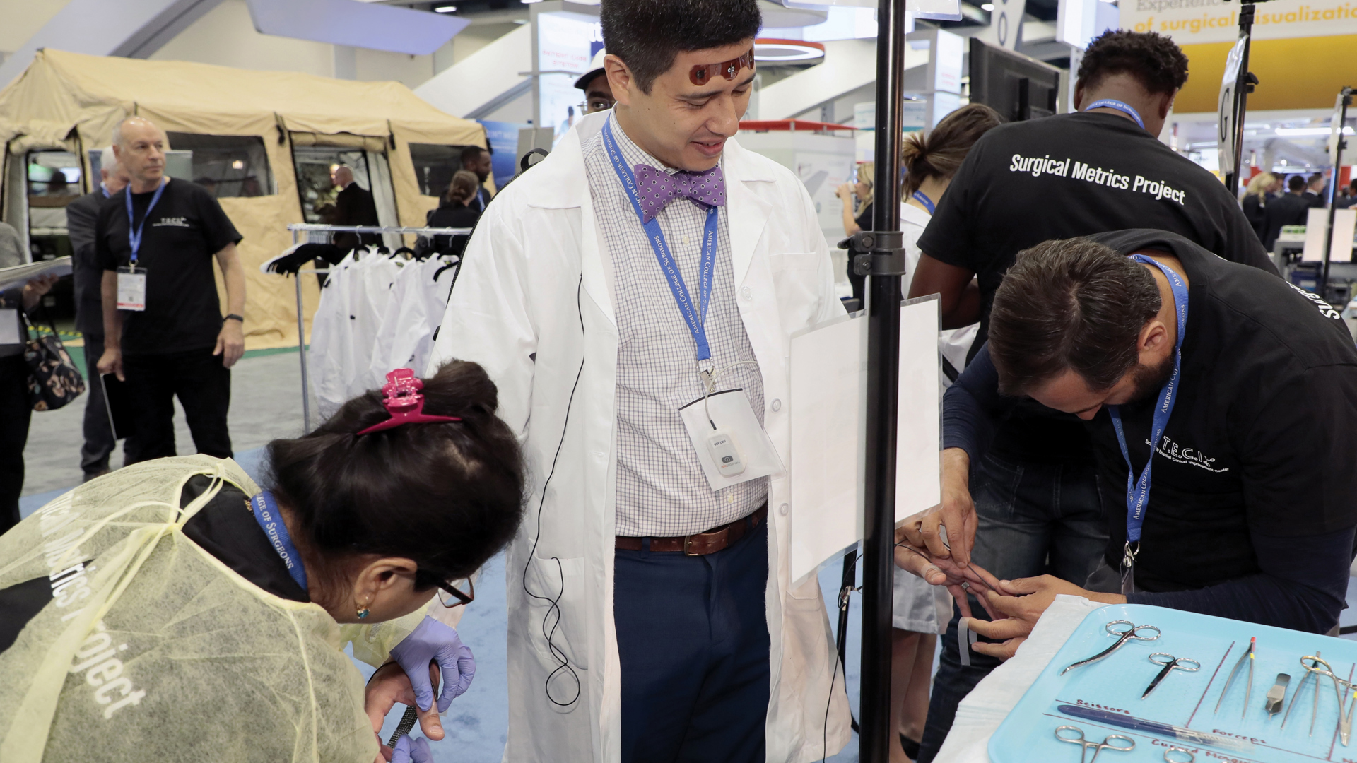 Surgical Metrics Project associates help a participant apply hand and fingers sensors used to track movements while completing a operation simulation.